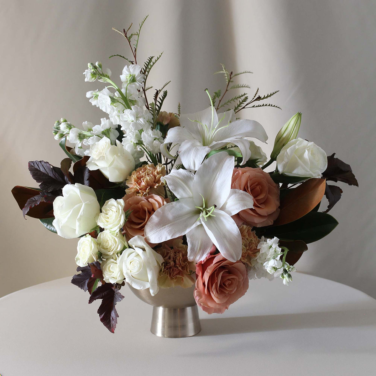 Endless Grace floral arrangement by Flower to Table featuring peach, blush and creamy white blooms with rich foliage, artfully designed in an elegant compote vase for Scottsdale flower delivery.